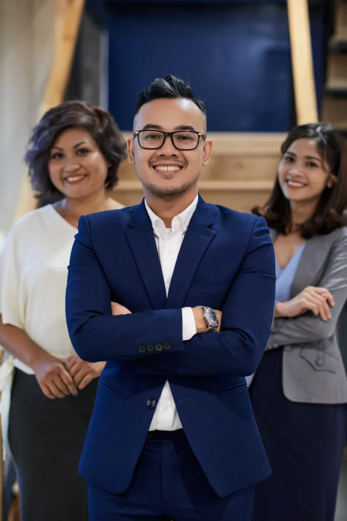 confident asian businessman posing with crossed arms two female colleagues standing